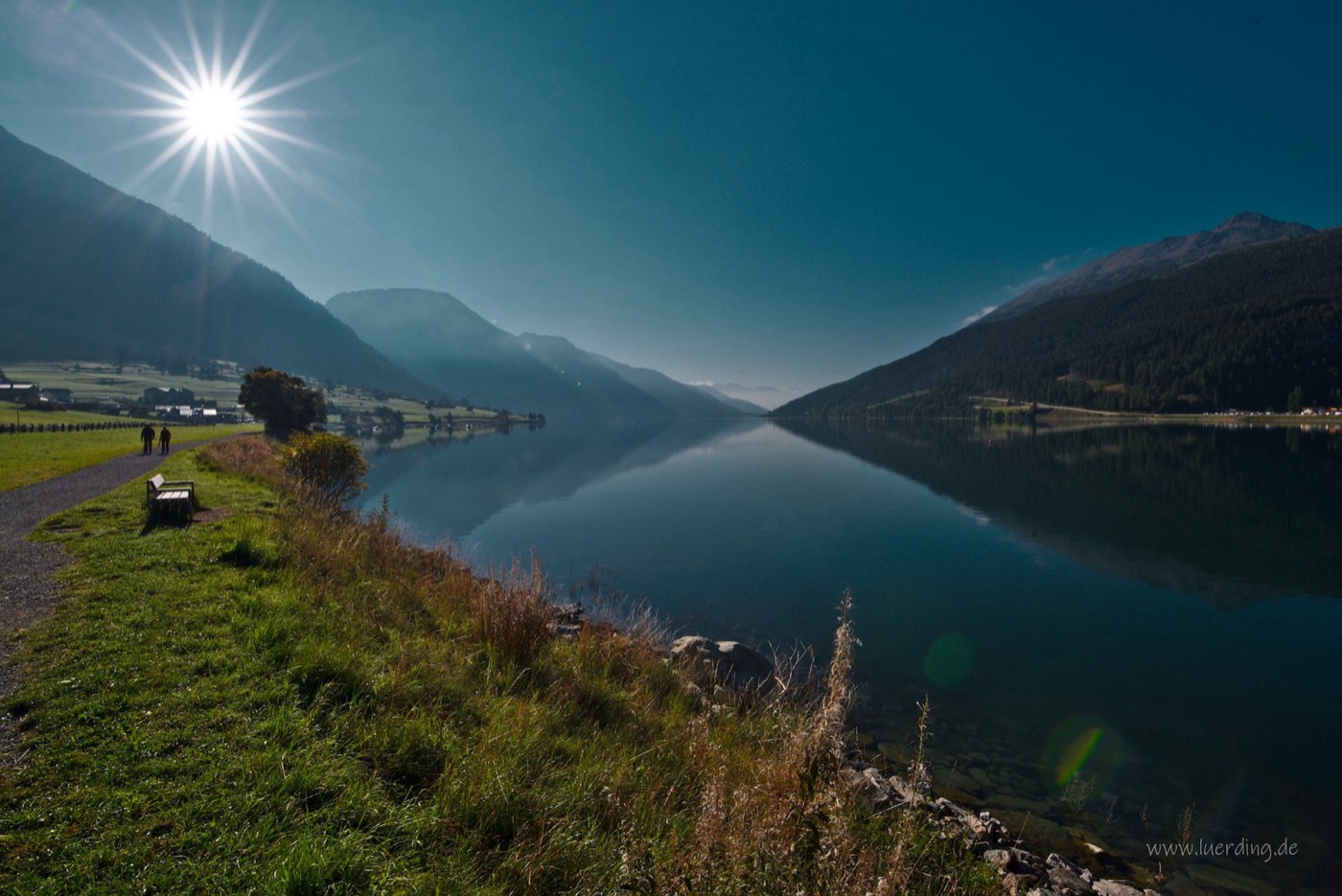 Still mountain lake reflecting the sky, sun breaking through the trees