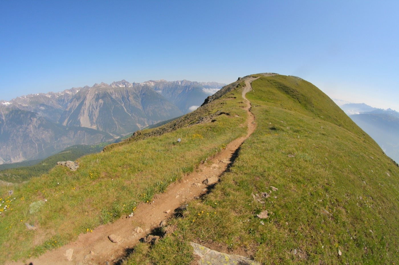 Wanderer auf einem begrünten Höhenweg über dem Tal